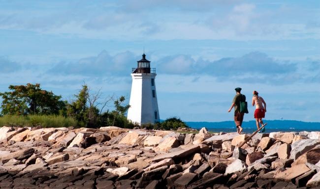 The essence of exceptional living two people walking on a rocky beach with Crisp Point Light in the background