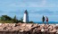 two people walking on a rocky beach with Crisp Point Light in the background