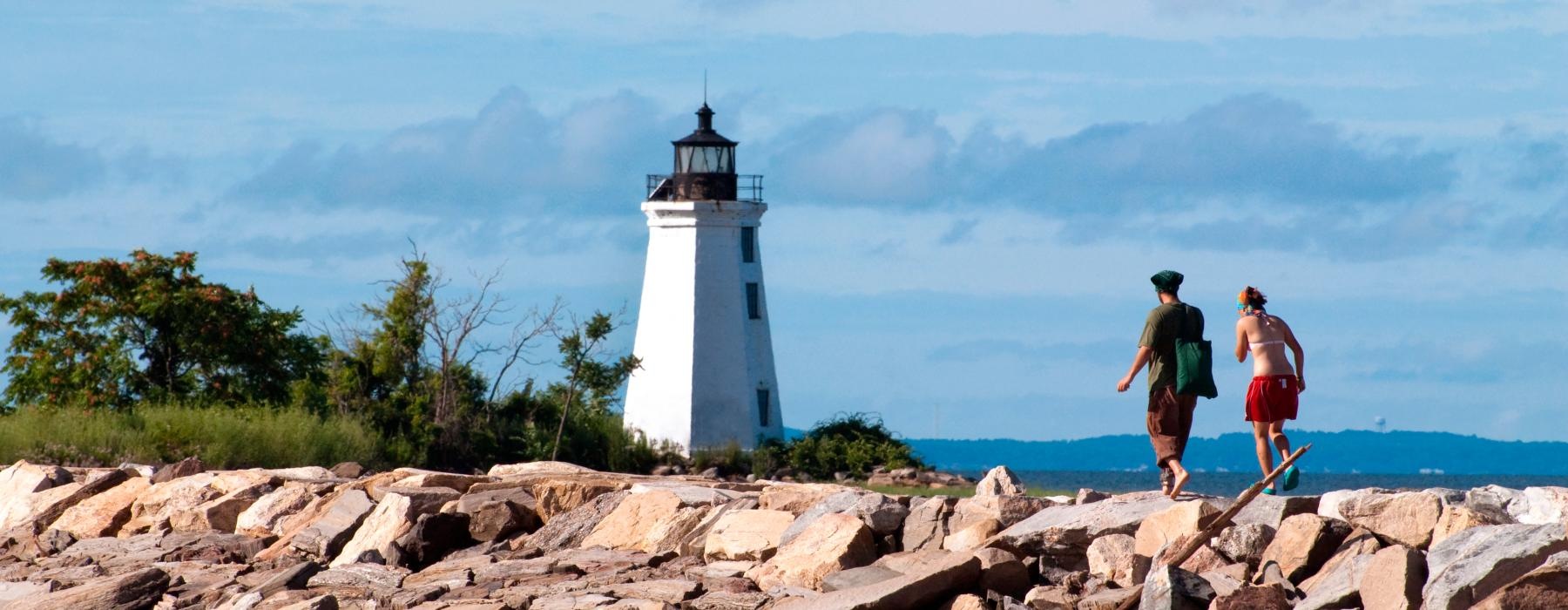 two people walking on a rocky beach with Crisp Point Light in the background